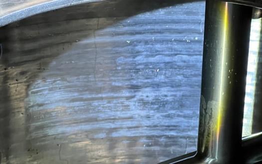 Tank wall under chlorinated alkaline CIP: streaked white film across the stainless surface.